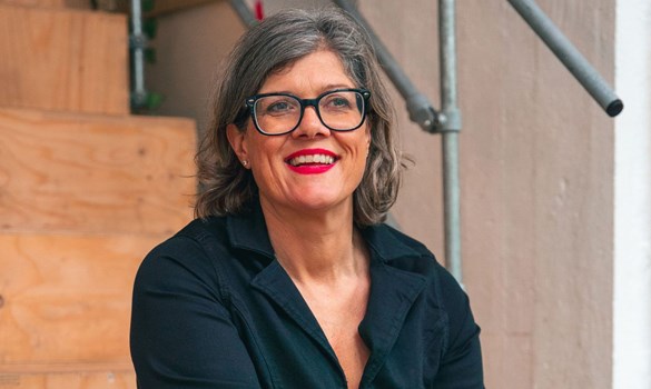Woman smiling sat on wooden steps wearing dark shirt and dark-rimmed glasses